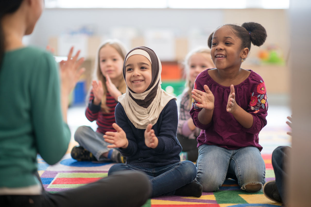 Preschool students singing and clapping along with their teacher