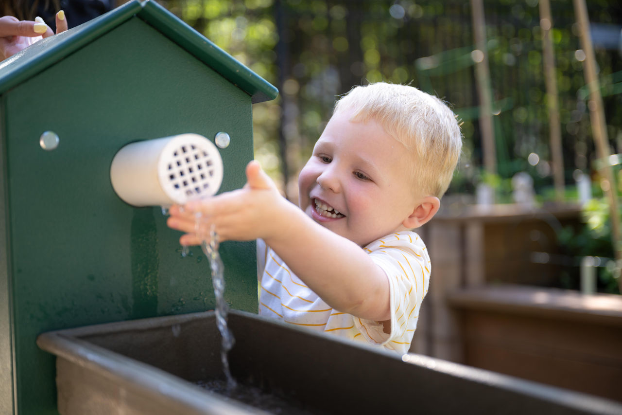A young boy playing with a water feature in an outdoor classroom at preschool