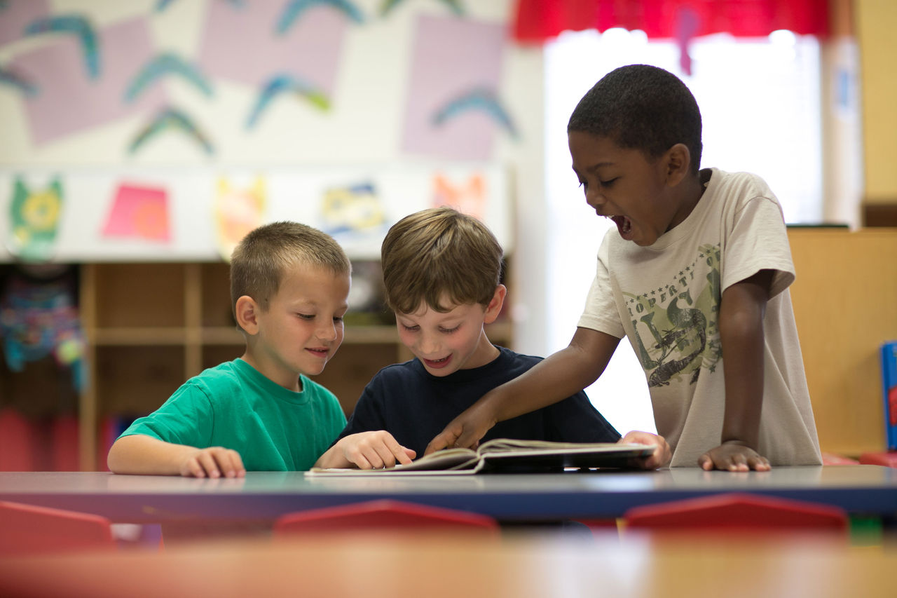 Three kindergarten students read a book together happily